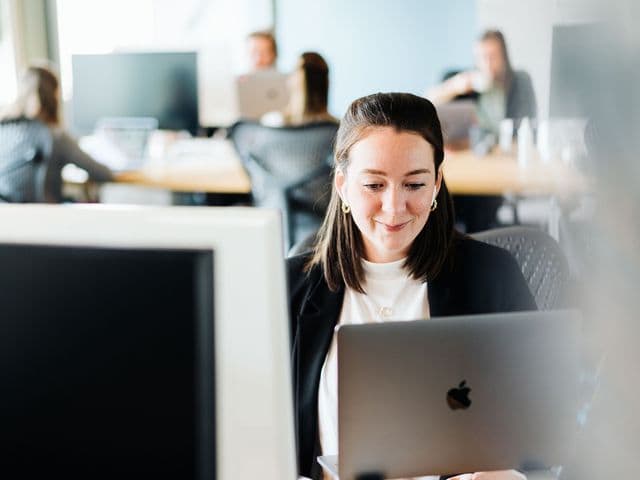 Eine unserer Kolleg+innen bei der Bildschirmarbeit im Büro, lächelnd. u+i interact