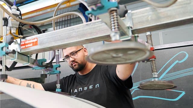 A man operates industrial machinery with suction cups in a workshop, focusing intently on the task.