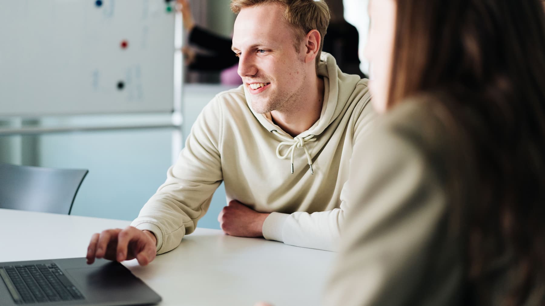 Zwei Menschen sitzen vor einem Laptop. Eine Person zeigt und erklärt der anderen Person etwas.