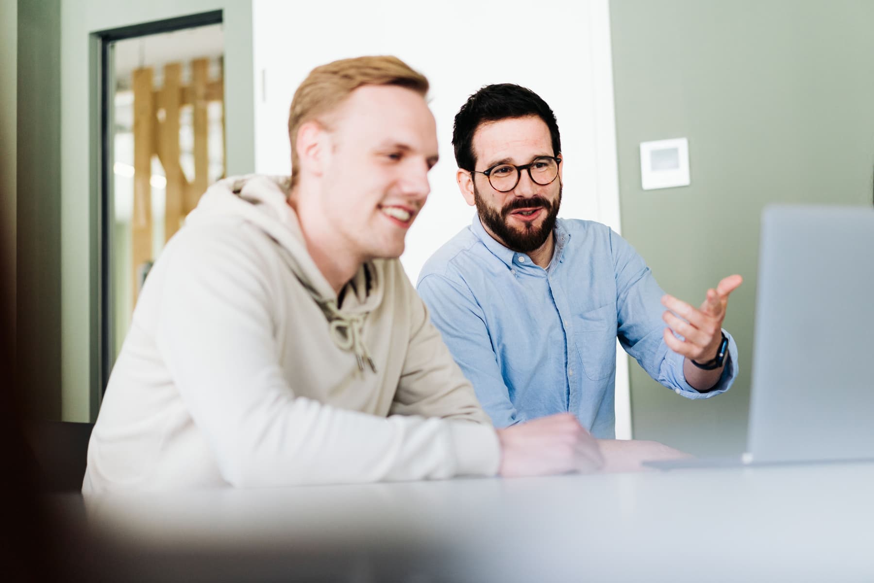 Zwei Kollegen schauen gemeinsam auf den Bildschirm und haben Spaß bei der Arbeit. u+i interact