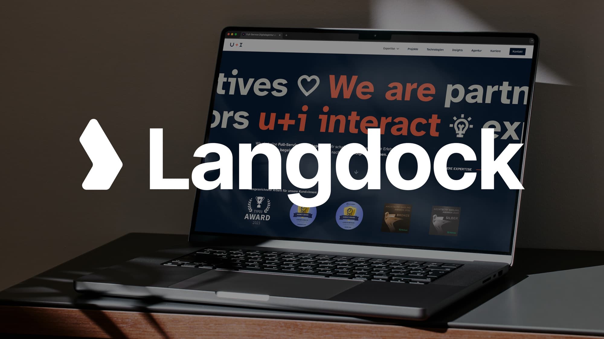 Ein aufgeklappter Laptop zeigt die Website von u+i interact mit dem Schriftzug „We are partners". Im Vordergrund ist das weiße Langdock-Logo eingeblendet – als Symbol für die Partnerschaft zwischen u+i interact und Langdock.