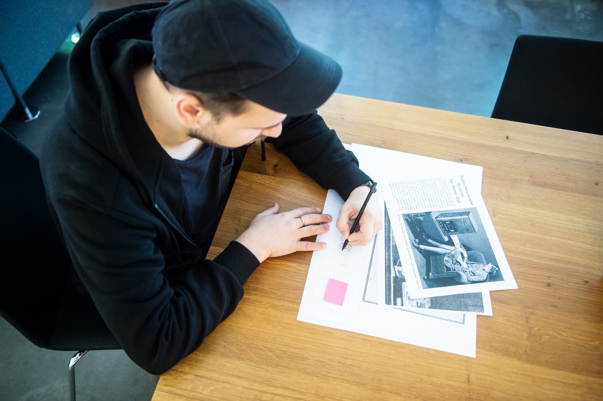 Blick von oben auf einen unserer Art Director+innen, der an einem Bürotisch sitzt und per Hand eine Zeichnung anfertigt. u+i interact