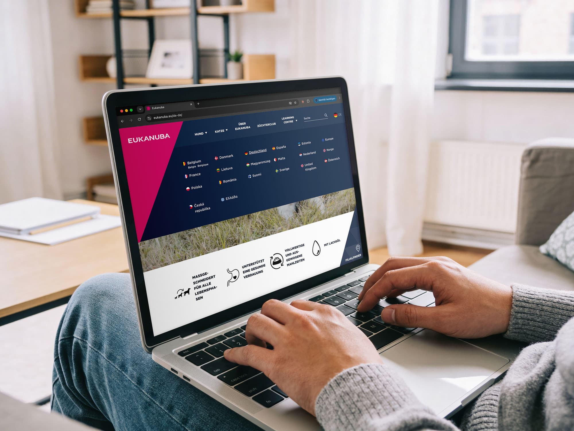 Person nutzt einen Laptop mit geöffneter Eukanuba-Website, auf der eine Auswahl europäischer Länder und Sprachversionen angezeigt wird.