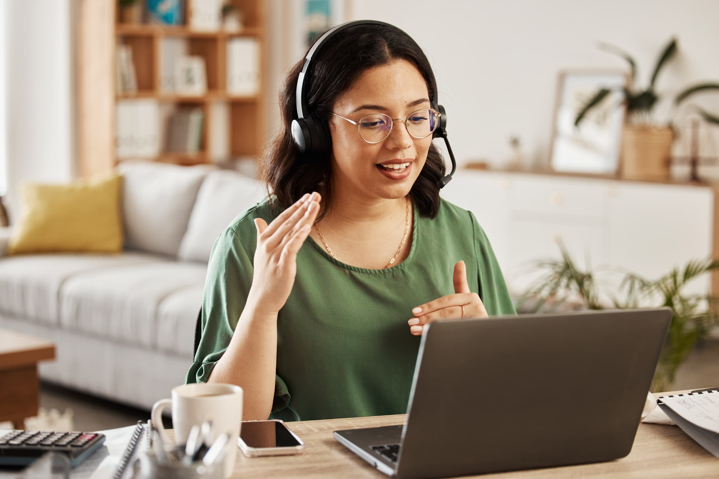 Frau mit Headset und Laptop im Homeoffice erklärt etwas über Videotelefonie.