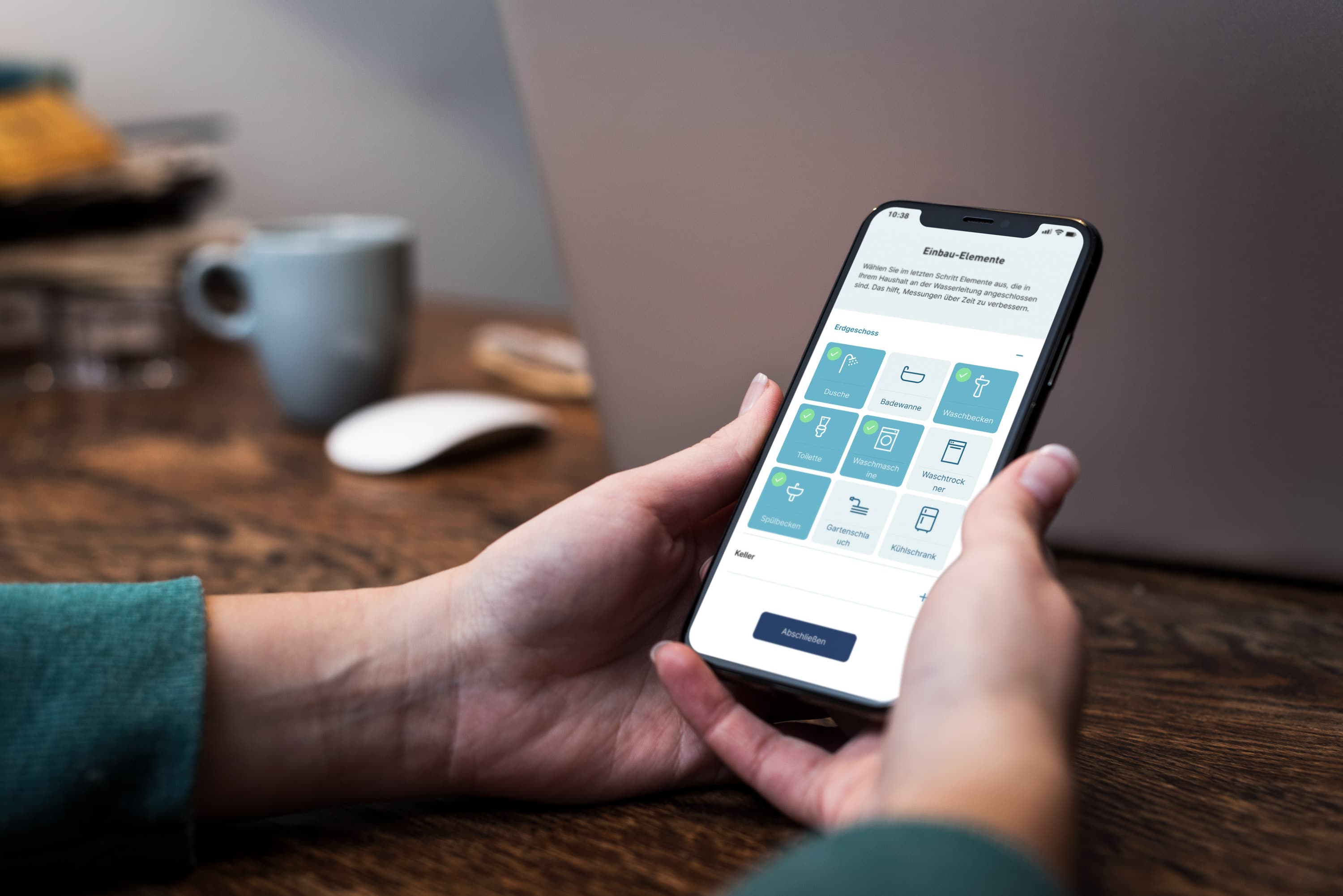 Eine Testperson hält ein Smartphone beiden Händen, auf dem ein Prototyp einer App zu sehen ist. Im Hintergrund stehen unscharf ein Laptop, eine Kaffeetasse und weitere Gegenstände auf einem Holztisch.
