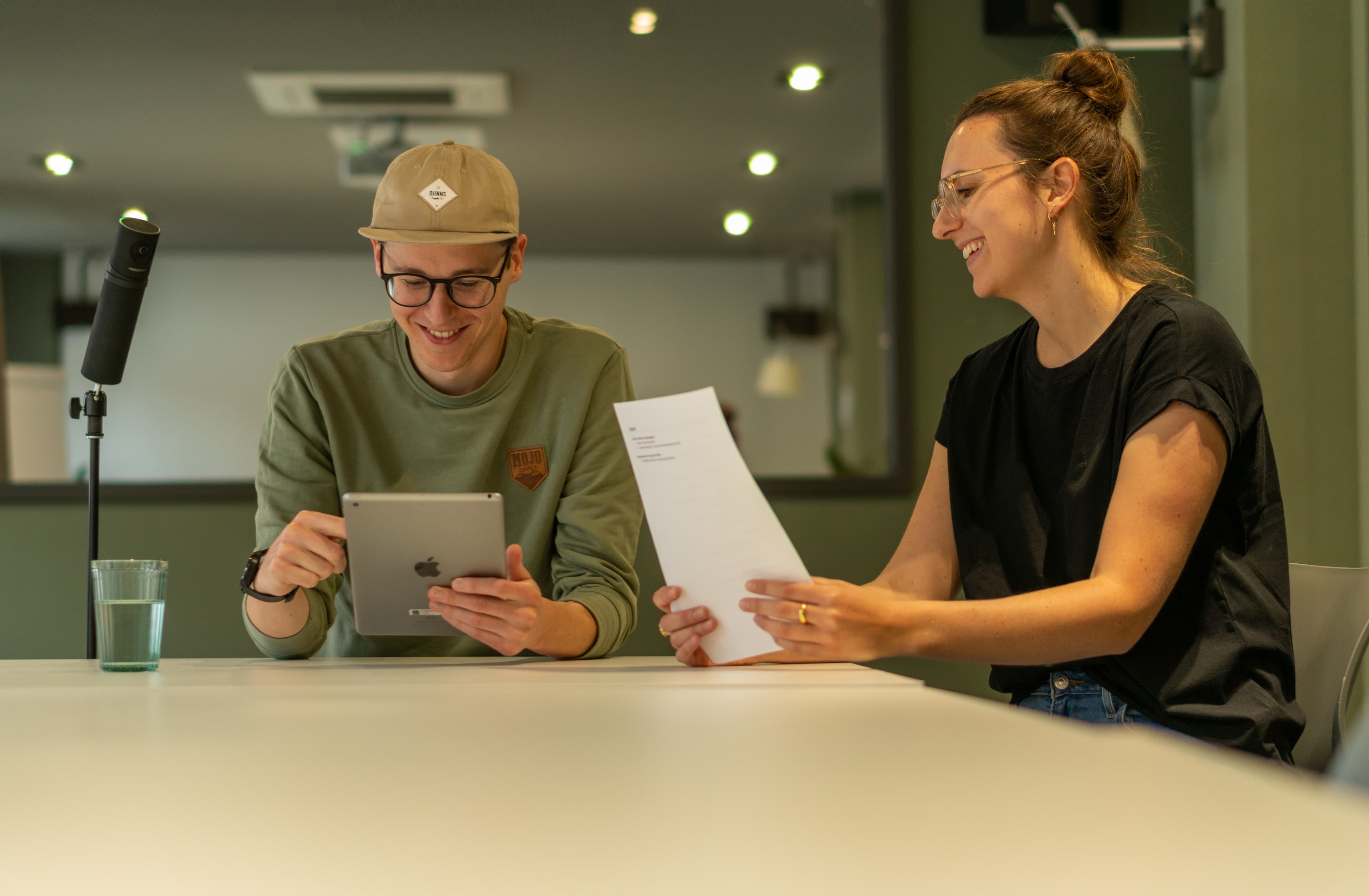 Zwei Kolleg+innen besprechen gut gelaunt ihre Notizen im Usability Teststudio. Ein Kollege blickt dabei auf ein Tablet, die Kollegin schaut auf ein Blatt Papier. u+i interact