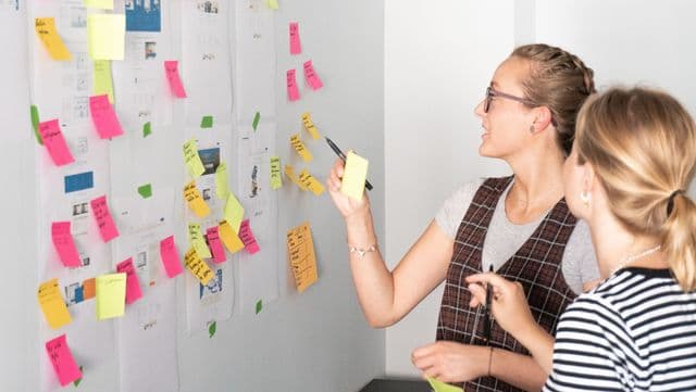 Hier sortieren zwei Kolleg+innen Notizen am Memo-Board in unserem Usability-Teststudio. u+i interact