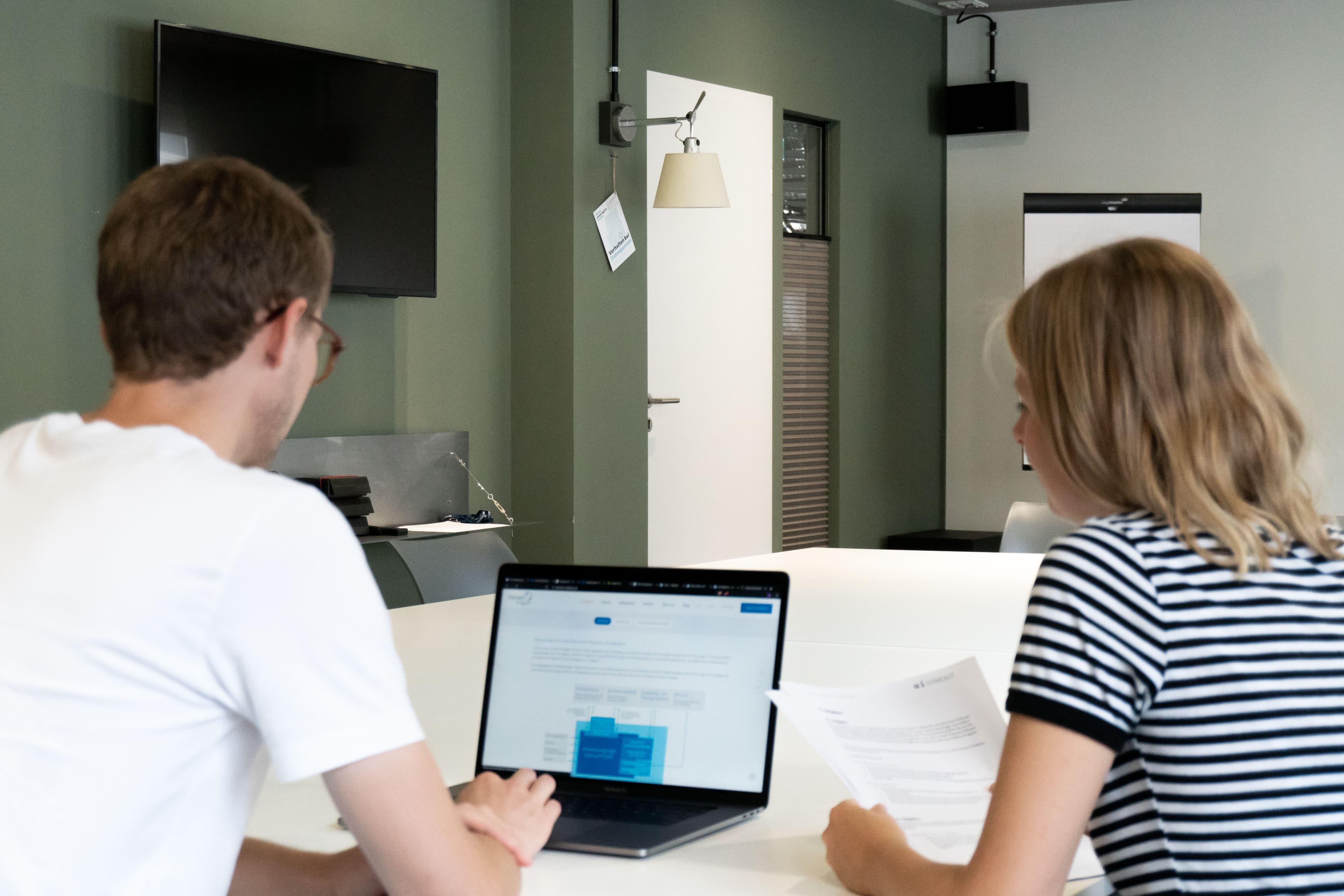 Zwei u+i Mitarbeiter:innen sind von hinten zu sehen, wie sie am Laptop ein UX Testing auswerten. u+i interact