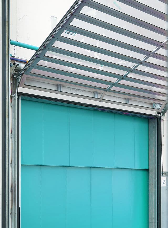 A turquoise industrial garage door is partially open, revealing a metal frame and ceiling with a modern, clean design.