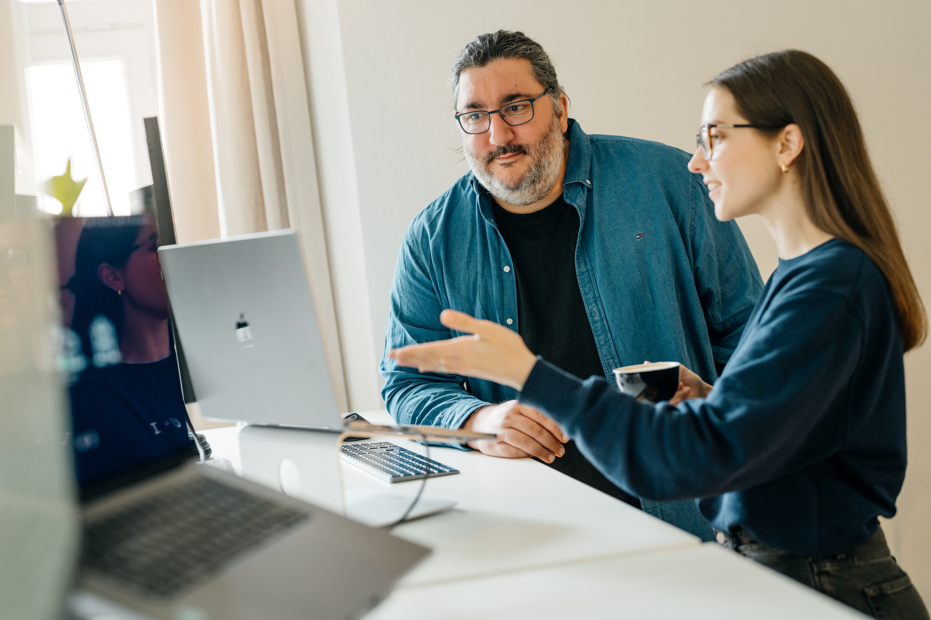 Zwei Personen schauen konzentriert auf einen Laptop, während eine weitere Person etwas darauf zeigt.