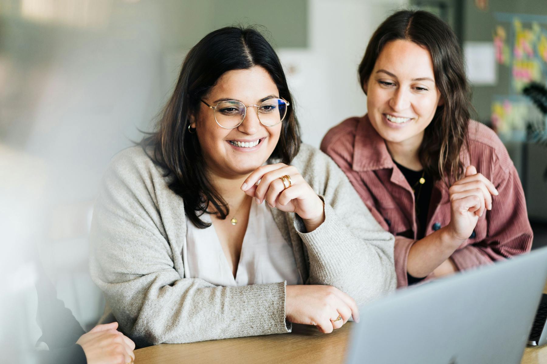 Zwei Kolleginnen schauen gemeinsam im Bielefelder Büro auf den Bildschirm eines Notebooks. Sie lächeln. u+i interact